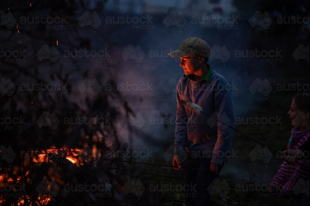 Boy cooks damper on bonfire - Australian Stock Image