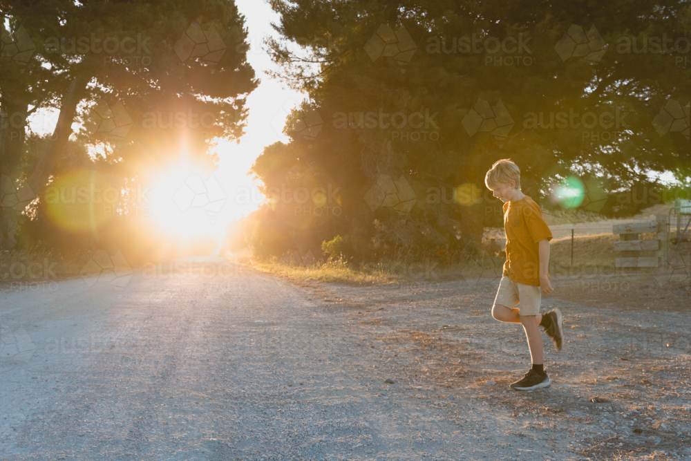 Boy crossing country dirt road at sunset - Australian Stock Image