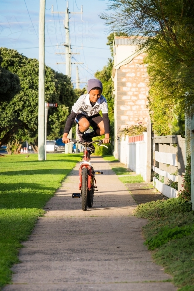 Boy doing tricks on his bike on the foot path in his street - Australian Stock Image