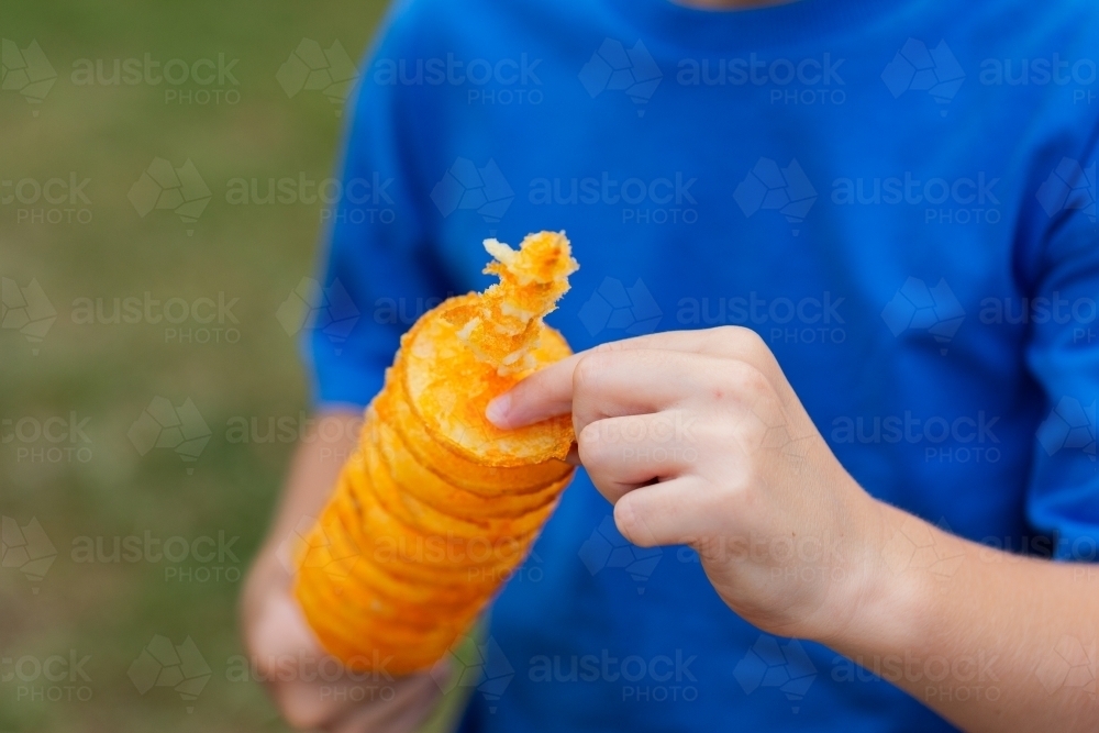 boy eating hot flavored chips on a stick – tornado potatoes - Australian Stock Image