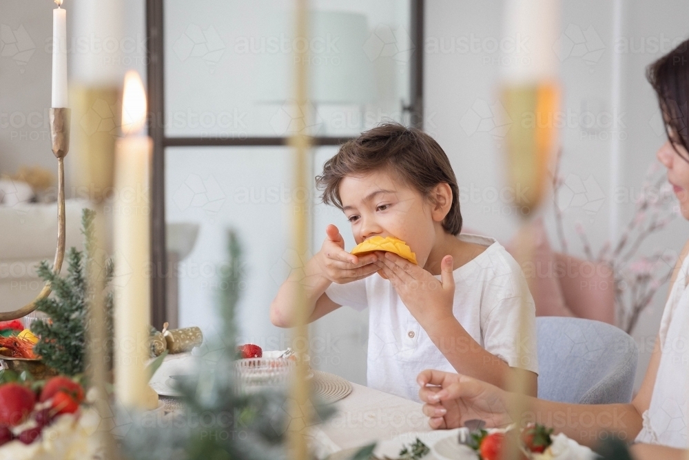 Boy eating slice of mango at christmas table - Australian Stock Image