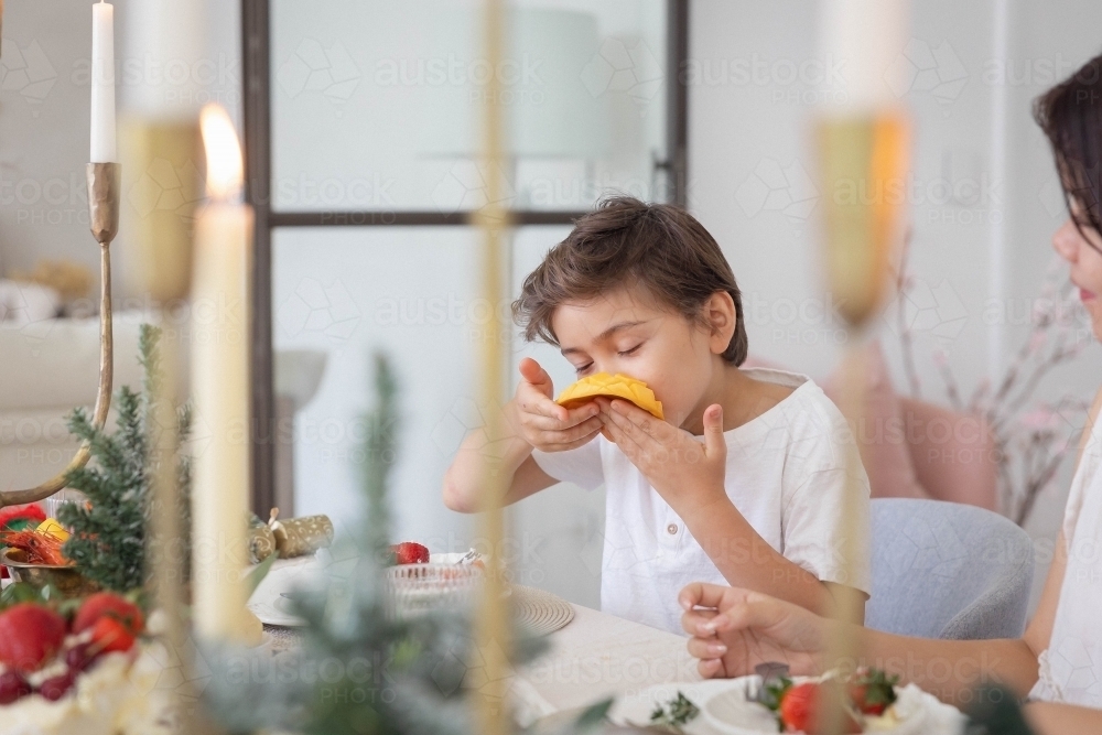 Boy eating slice of mango at christmas table - Australian Stock Image