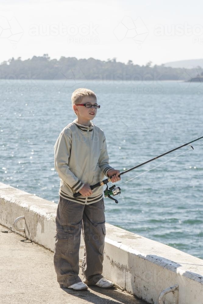 Boy fishing off wharf on a sunny day - Australian Stock Image