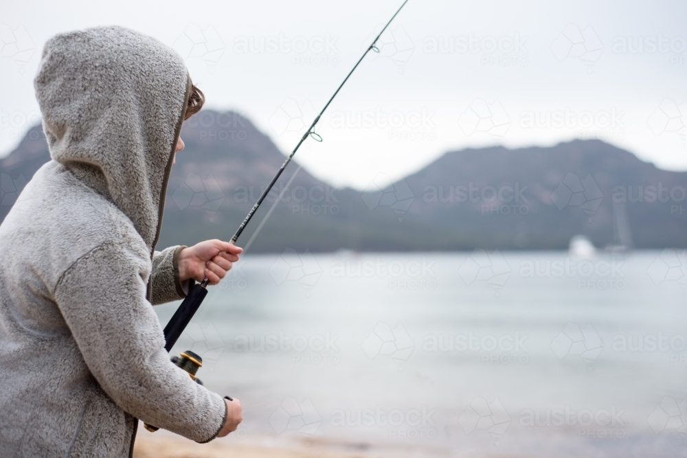 Boy fishing on a beach surrounded by mountains - Australian Stock Image