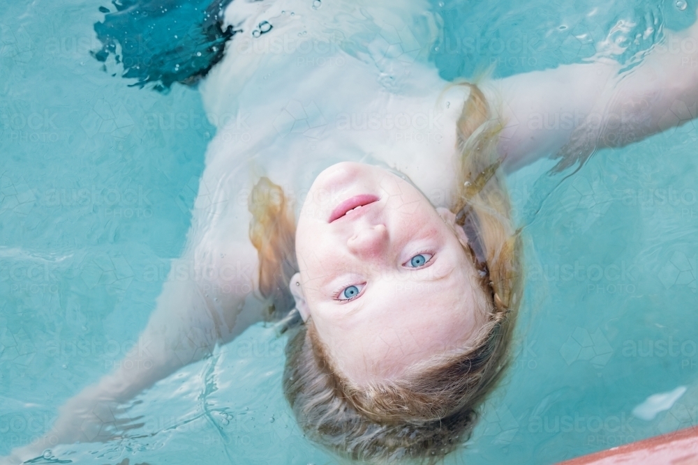 Image of Boy floating upside down in resort swimming pool, close up of ...