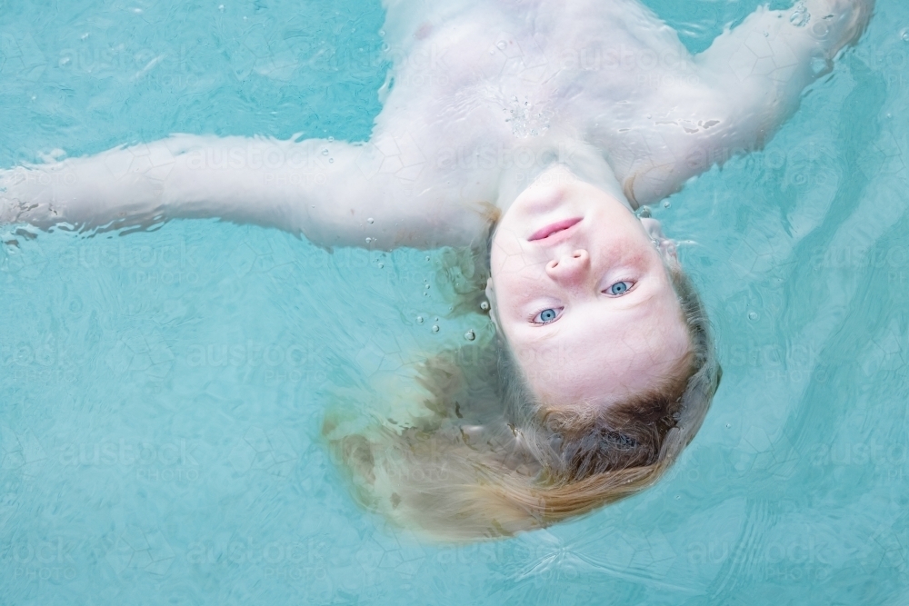 Boy floating upside down in resort swimming pool, close up of face - Australian Stock Image