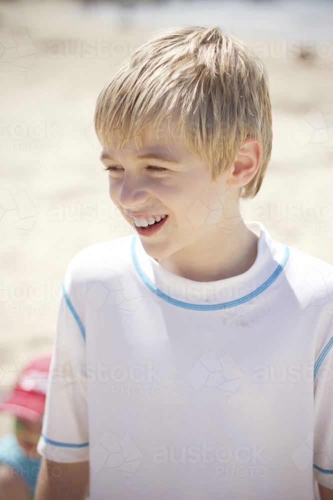 Boy grinning wearing rash vest at the beach - Australian Stock Image