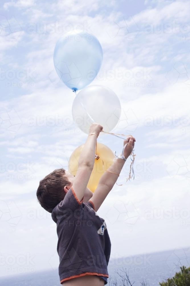 Boy holding bunch of coloured balloons looking up at them - Australian Stock Image