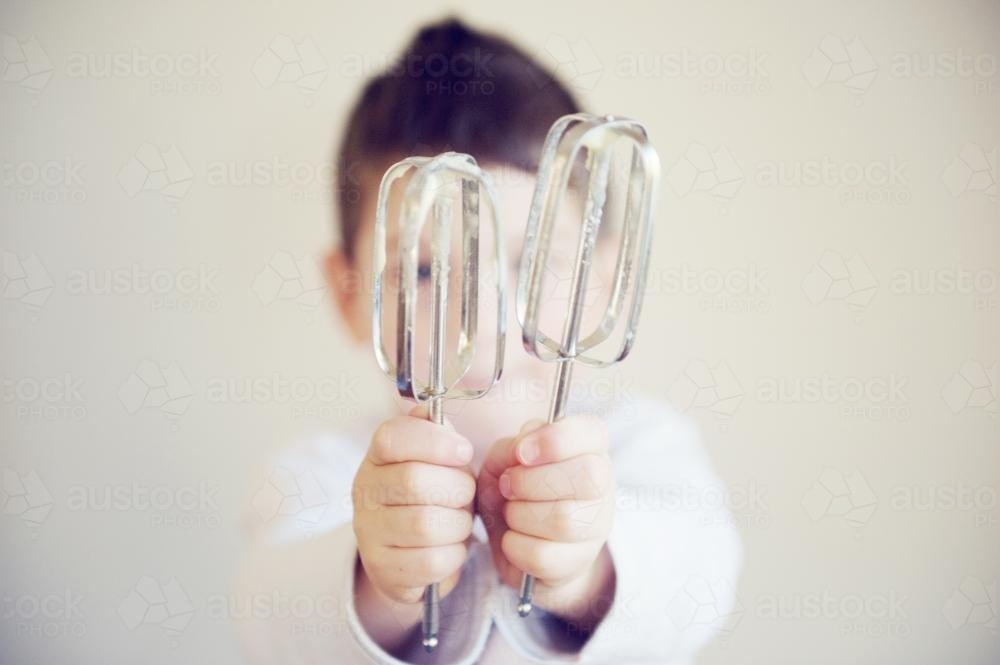 Boy holding cake beaters in front of his face - Australian Stock Image