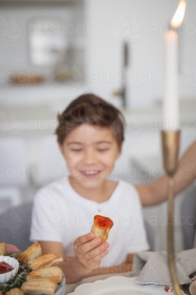 Boy holding pastry with tomato sauce at kitchen table - Australian Stock Image
