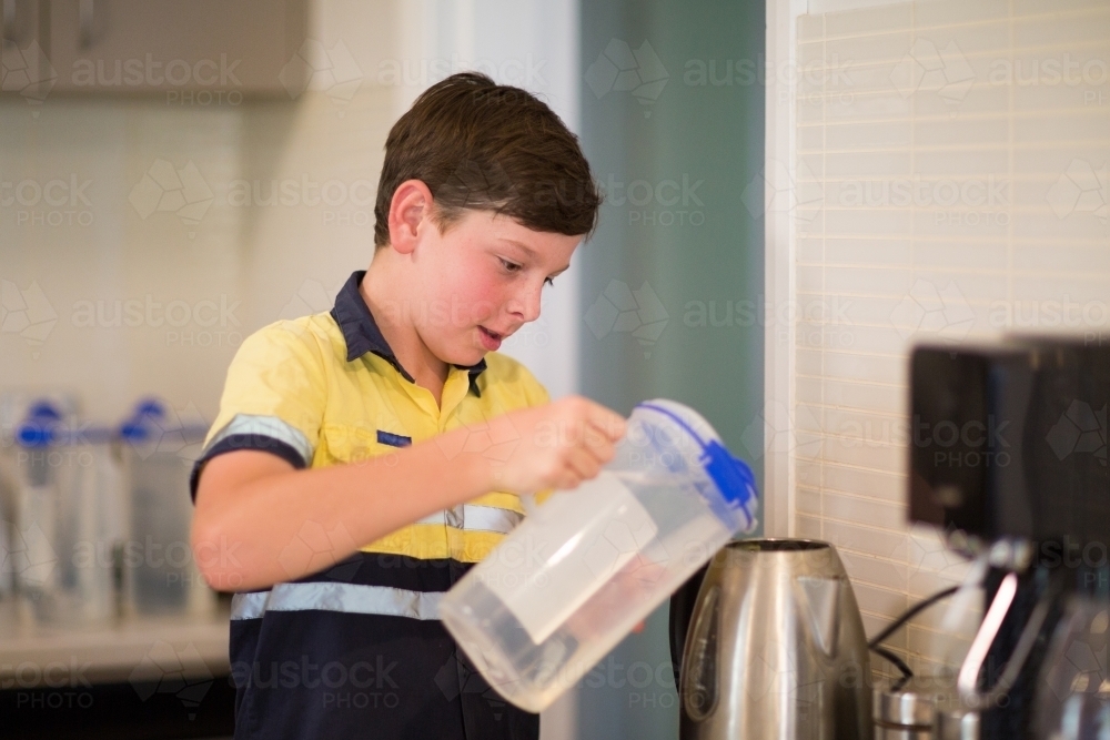Boy in kitchen filling kettle - Australian Stock Image