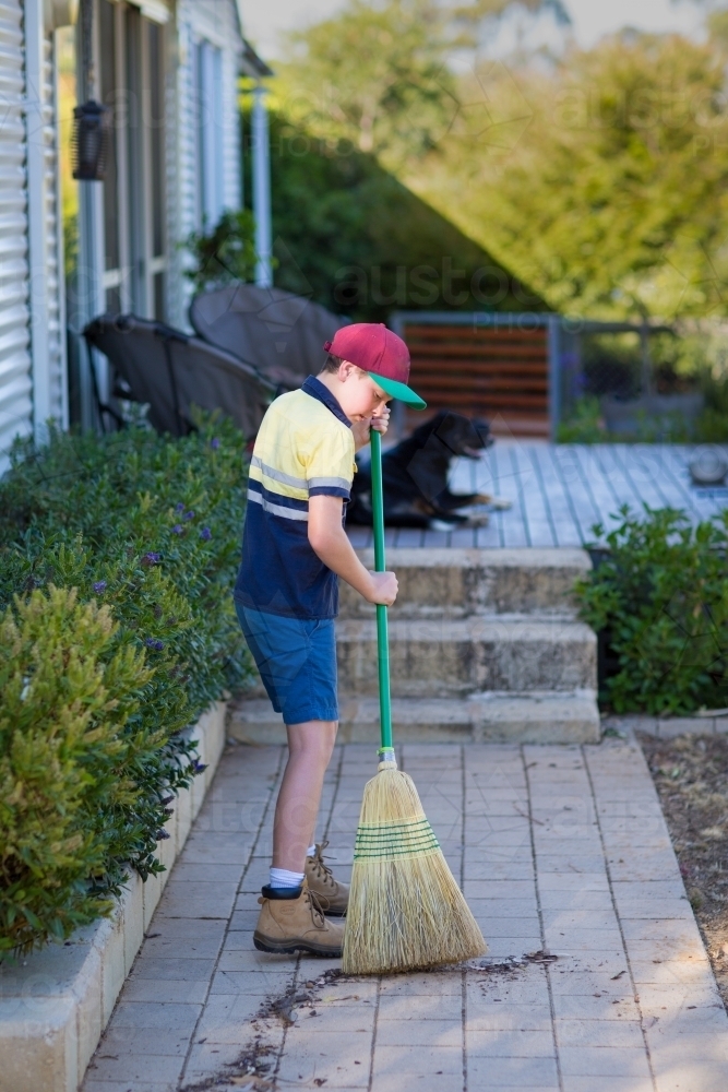 Boy in work clothes sweeping paved path - Australian Stock Image