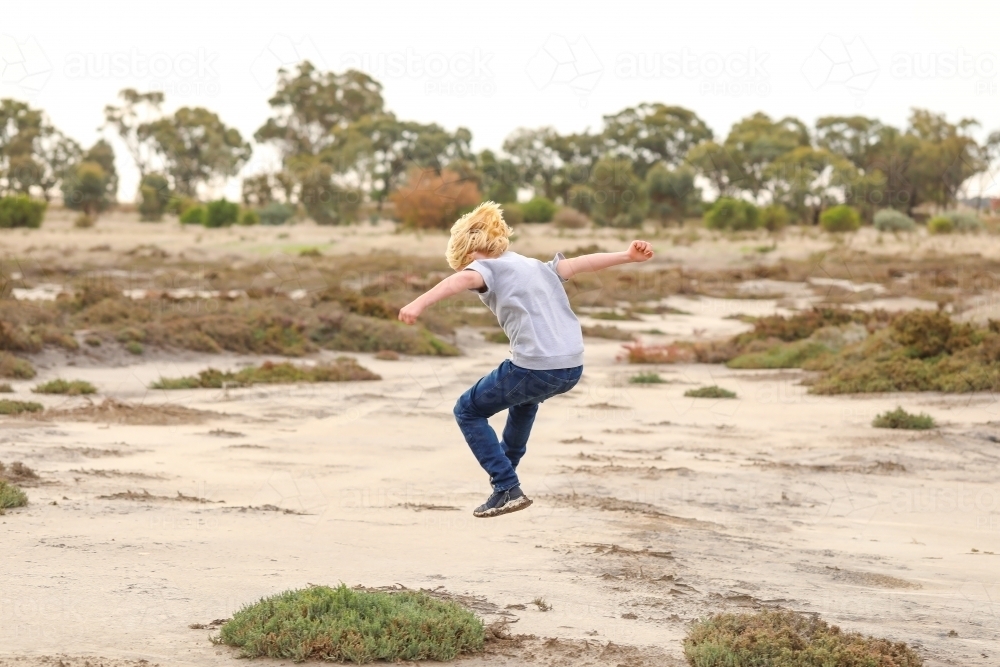 Boy jumping in the air while exploring dry lake in the Australian bush - Australian Stock Image