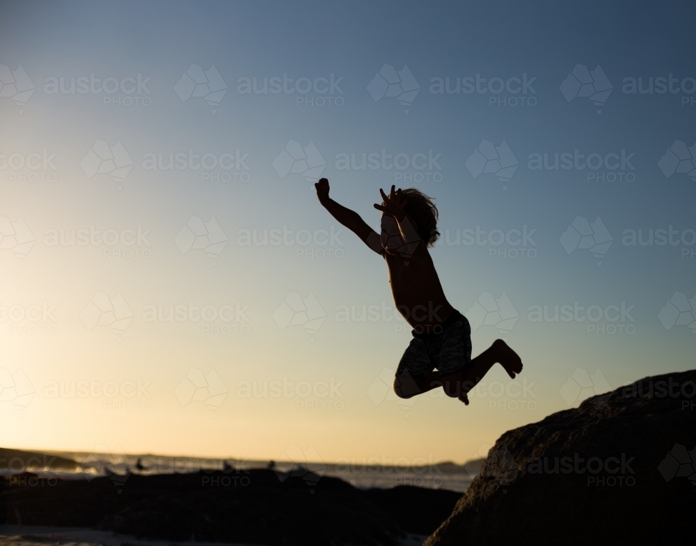 Boy jumping off a rock on the beach - Australian Stock Image