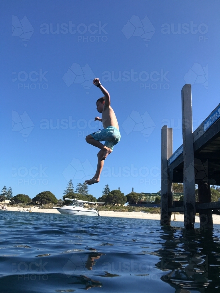 Boy jumping off jetty into river - Australian Stock Image