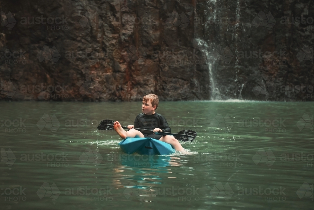 Boy kayaking with paddle in cool blue water at Cedar Creek Falls in the Whitsundays - Australian Stock Image