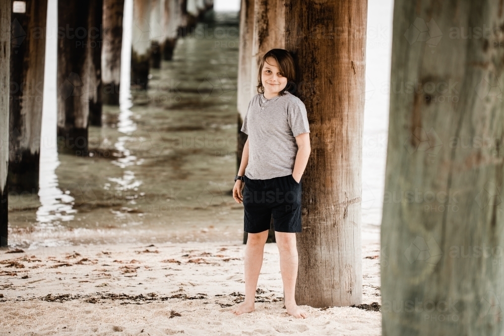 Boy leaning on a pier at the beach looking at the camera - Australian Stock Image