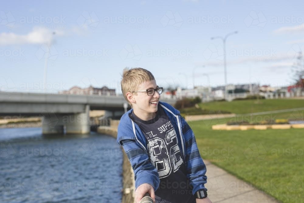 Boy leaning on fence near river - Australian Stock Image