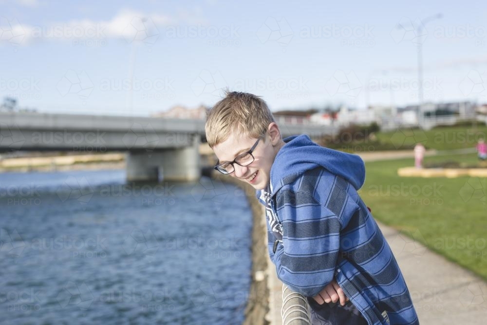 Boy leaning over fence near river - Australian Stock Image