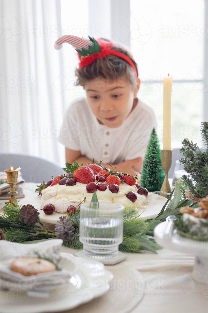 Boy looking at pavlova on Christmas decorated table - Australian Stock Image