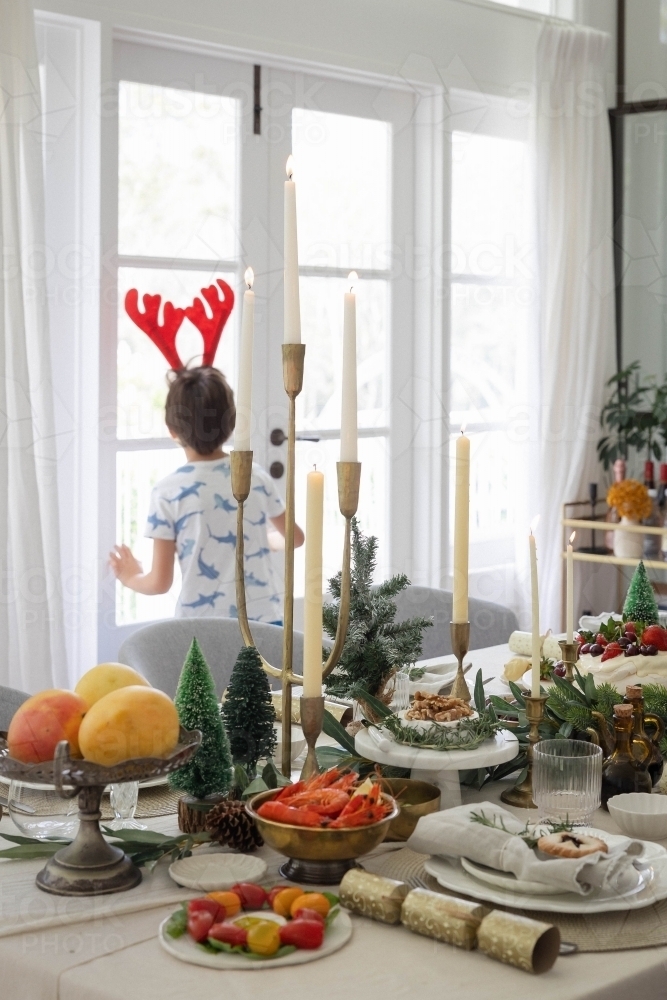 Boy looking out window with prepared Christmas meal in foreground - Australian Stock Image