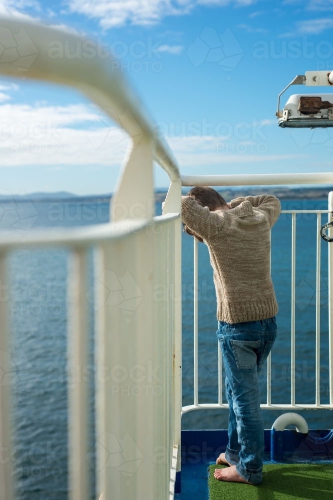 Boy looking through railing on a cruise ship at the ocean - Australian Stock Image