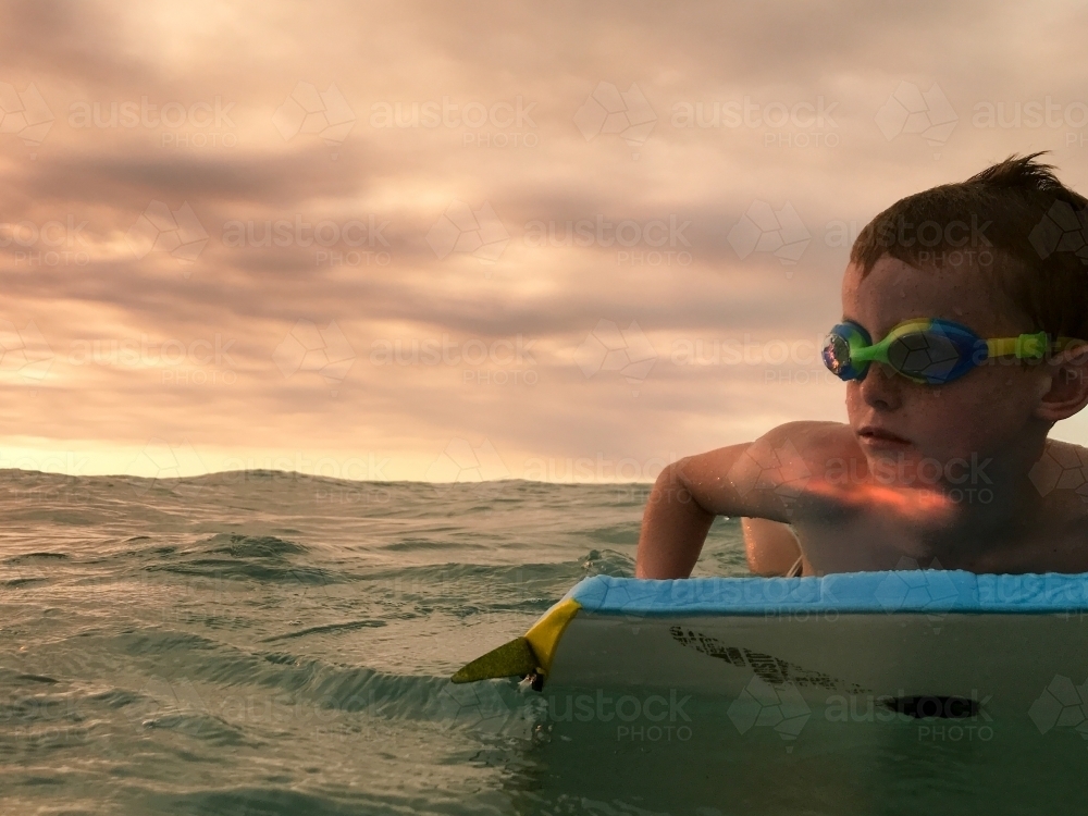 Boy on a bodyboard in the ocean at sunset - Australian Stock Image