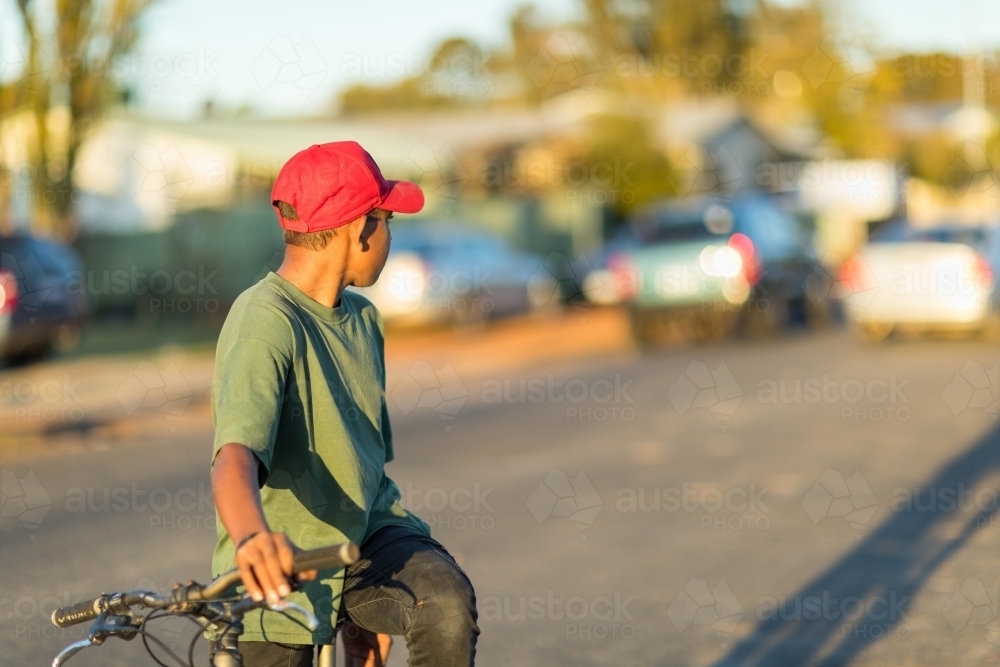 boy on bike looking over his shoulder back down the street - Australian Stock Image