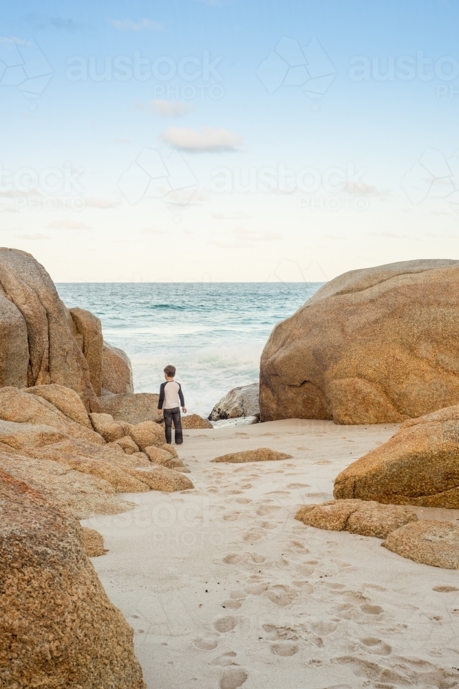 Boy on sandy beach surrounded by boulder rocks - Australian Stock Image