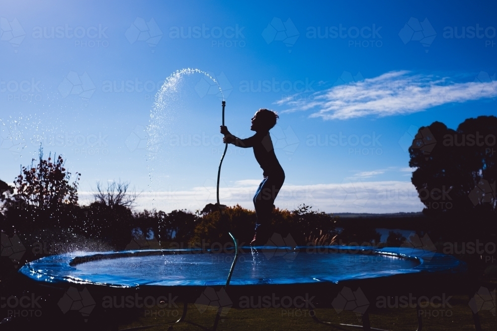 boy on trampoline with garden hose - Australian Stock Image