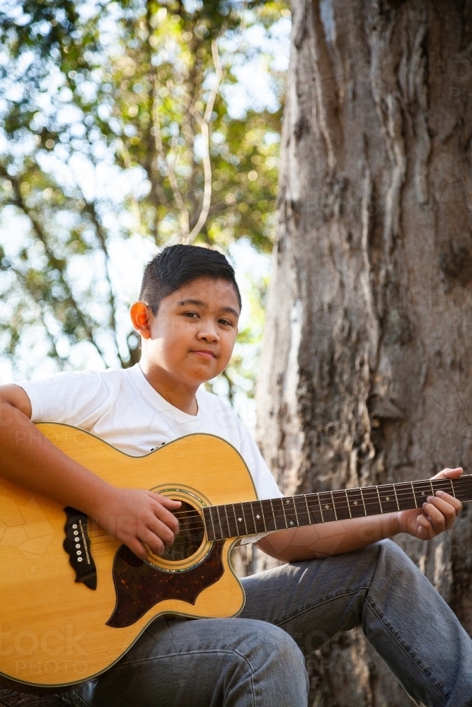Boy playing country music on acoustic guitar in bushland - Australian Stock Image