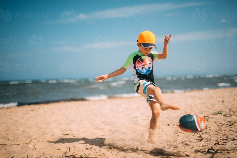 Boy playing football on the beach - Australian Stock Image