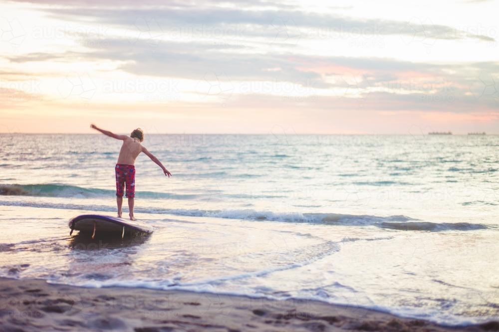 Boy playing on a SUP board at the beach at sunset - Australian Stock Image