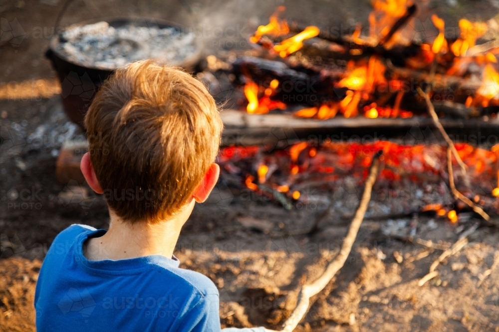 Image of Boy poking stick in campfire - Austockphoto