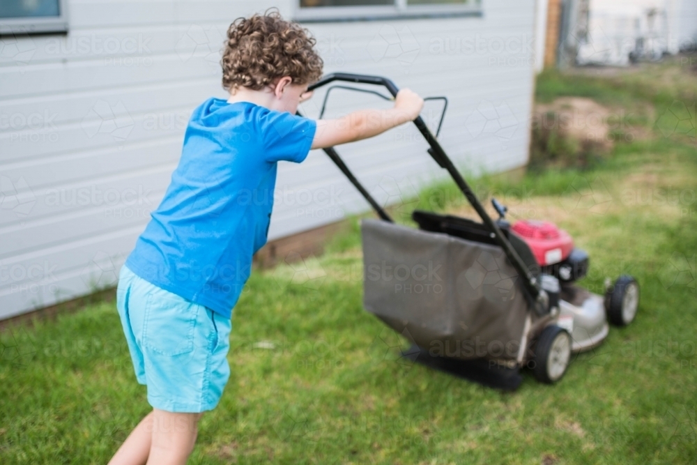 Boy pushing lawn mower mowing lawn - Australian Stock Image