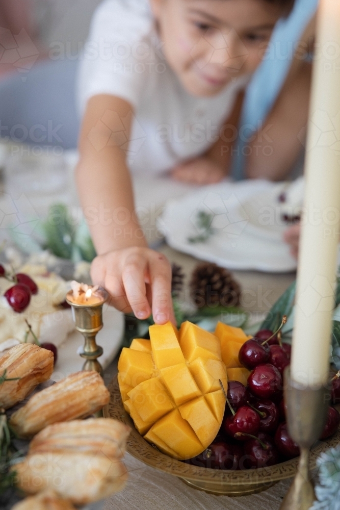 Boy reaching to grab slice of mango from bowl - Australian Stock Image