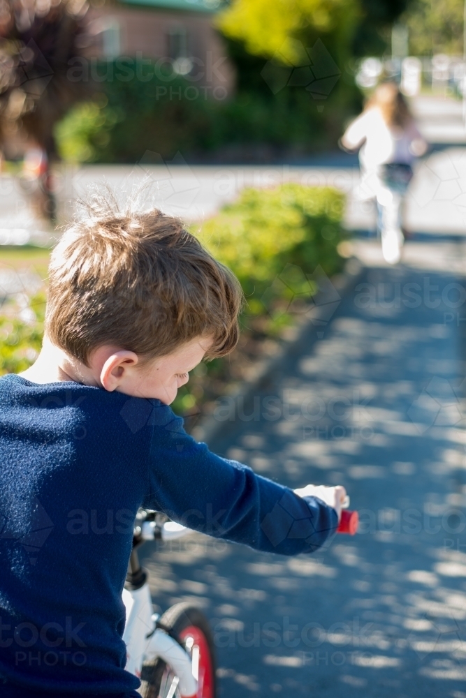 Boy riding a bike following girl on road - Australian Stock Image