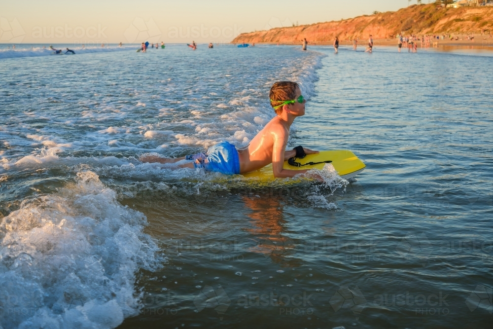 Boy riding bodyboard while wearing swimming goggles on the beach at sunset in South Australia - Australian Stock Image