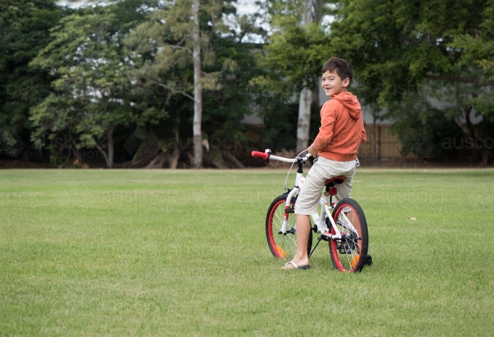 Boy riding orange bicycle on lawn. - Australian Stock Image