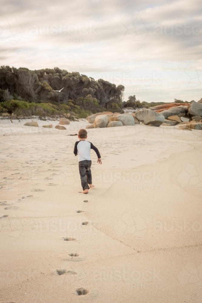 Image of Boy running along beach leaving footprints Austockphoto
