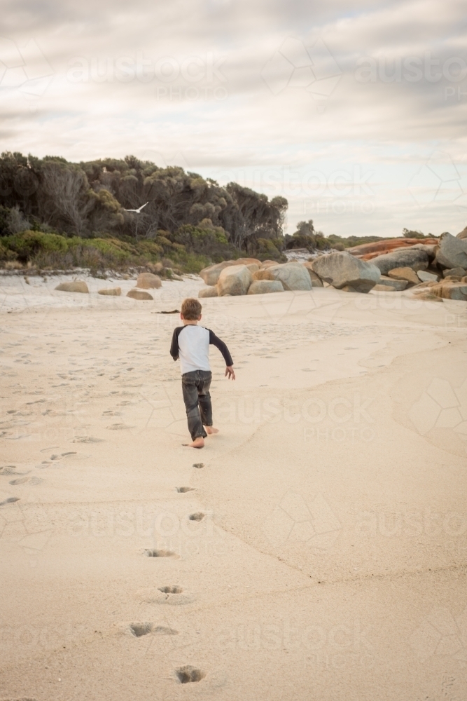 Boy running along beach leaving footprints - Australian Stock Image