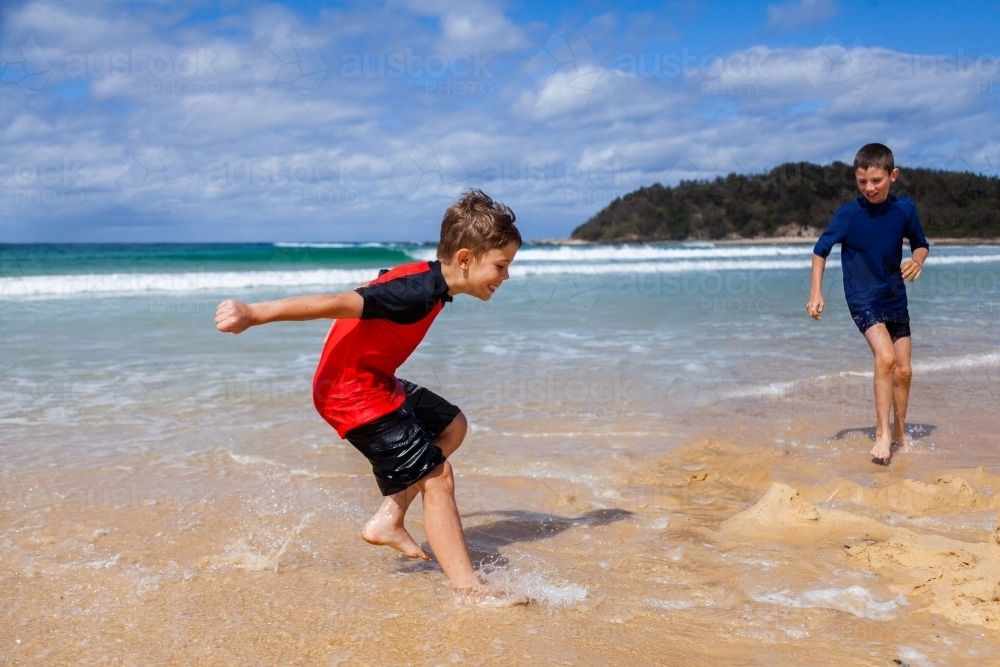 Boy running and splashing in the ocean waves at the beach - Australian Stock Image