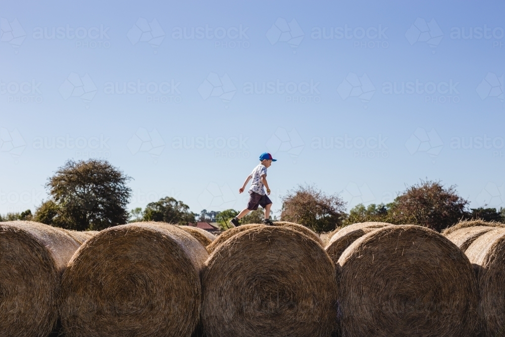 Boy running over the top of hay bales - Australian Stock Image