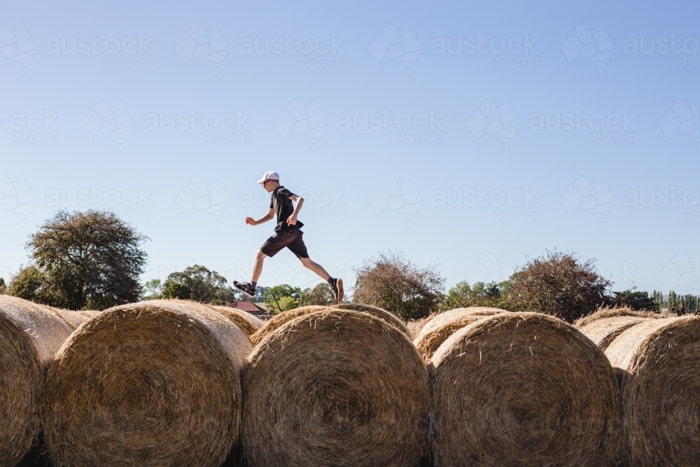 Boy running over the top of hay bales - Australian Stock Image