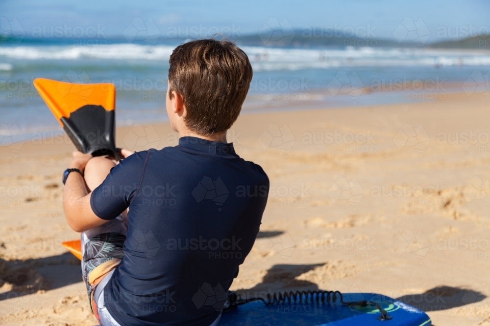 Boy seated on body board preparing to get into the sea - Australian Stock Image