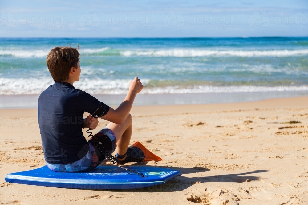 Boy seated on body board preparing to get into the sea - Australian Stock Image