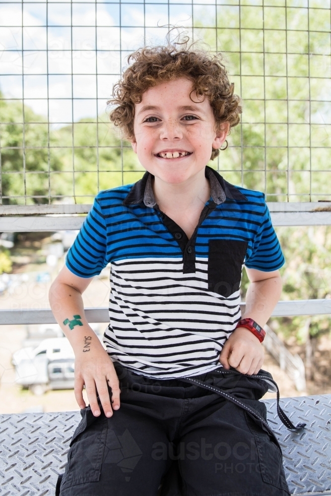 Boy sitting in ferris wheel cage at local show smiling - Australian Stock Image