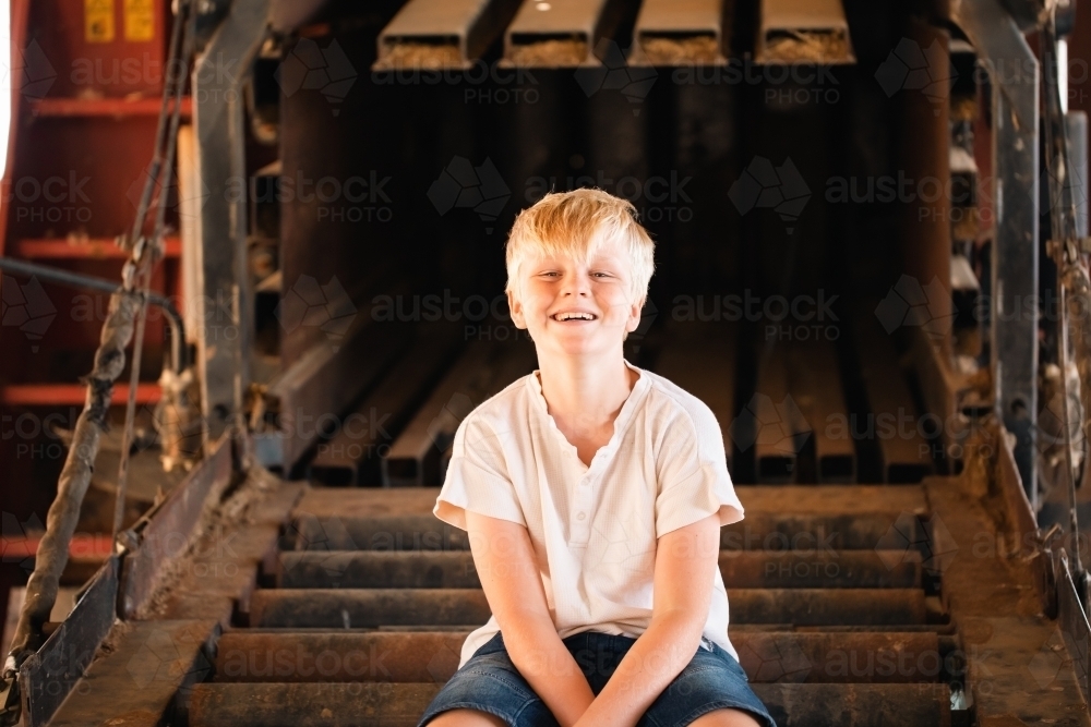 Image of Boy sitting on farm machinery in country shed - Austockphoto