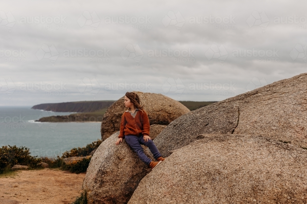 Boy sitting on large rock with ocean behind - Australian Stock Image
