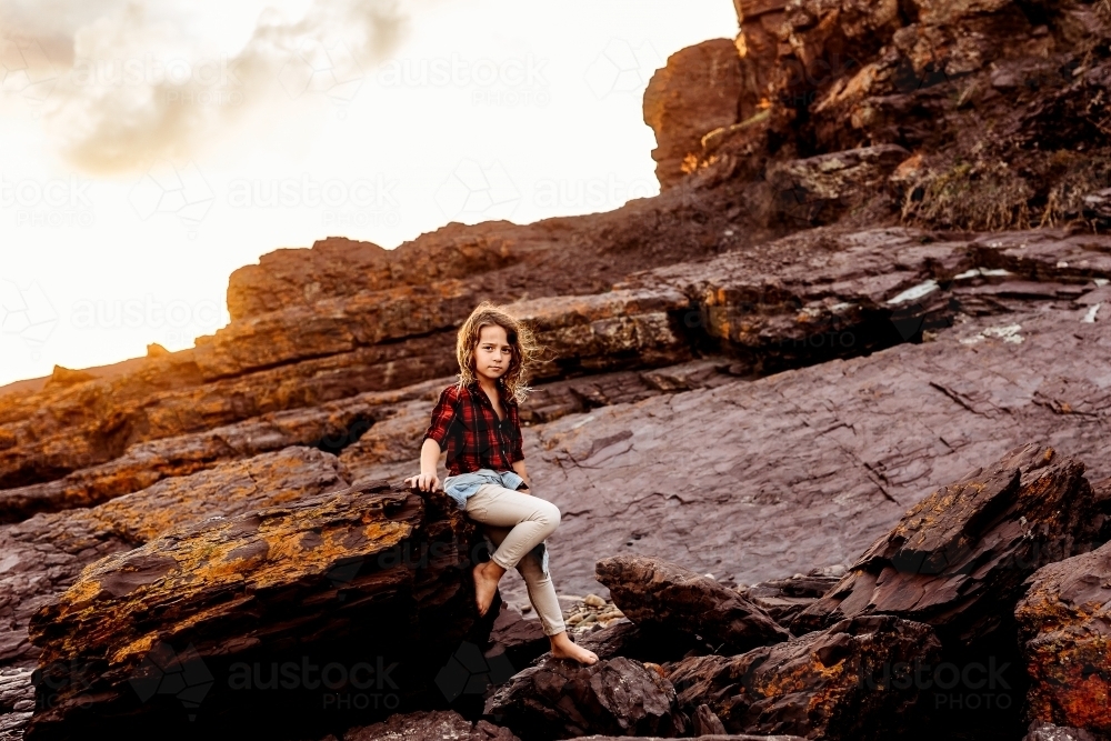 Boy sitting on rocks at sunset - Australian Stock Image